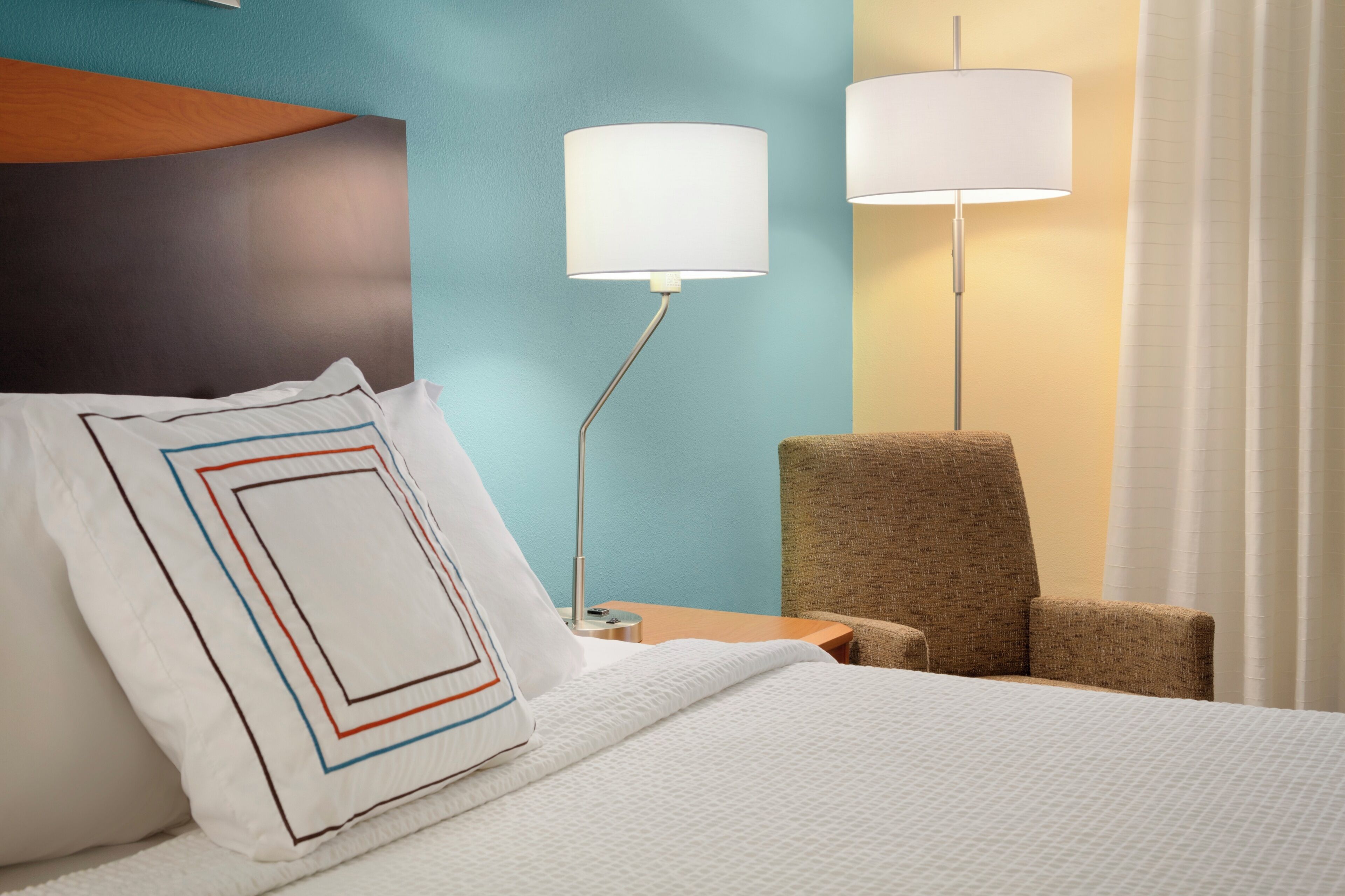 Ein Hotelzimmer mit einem Bett, einem Sessel, zwei Lampen und einem Nachttisch.