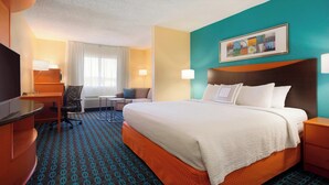 Quarto de hotel com uma cama grande, uma escrivaninha, uma cadeira e uma televisão.