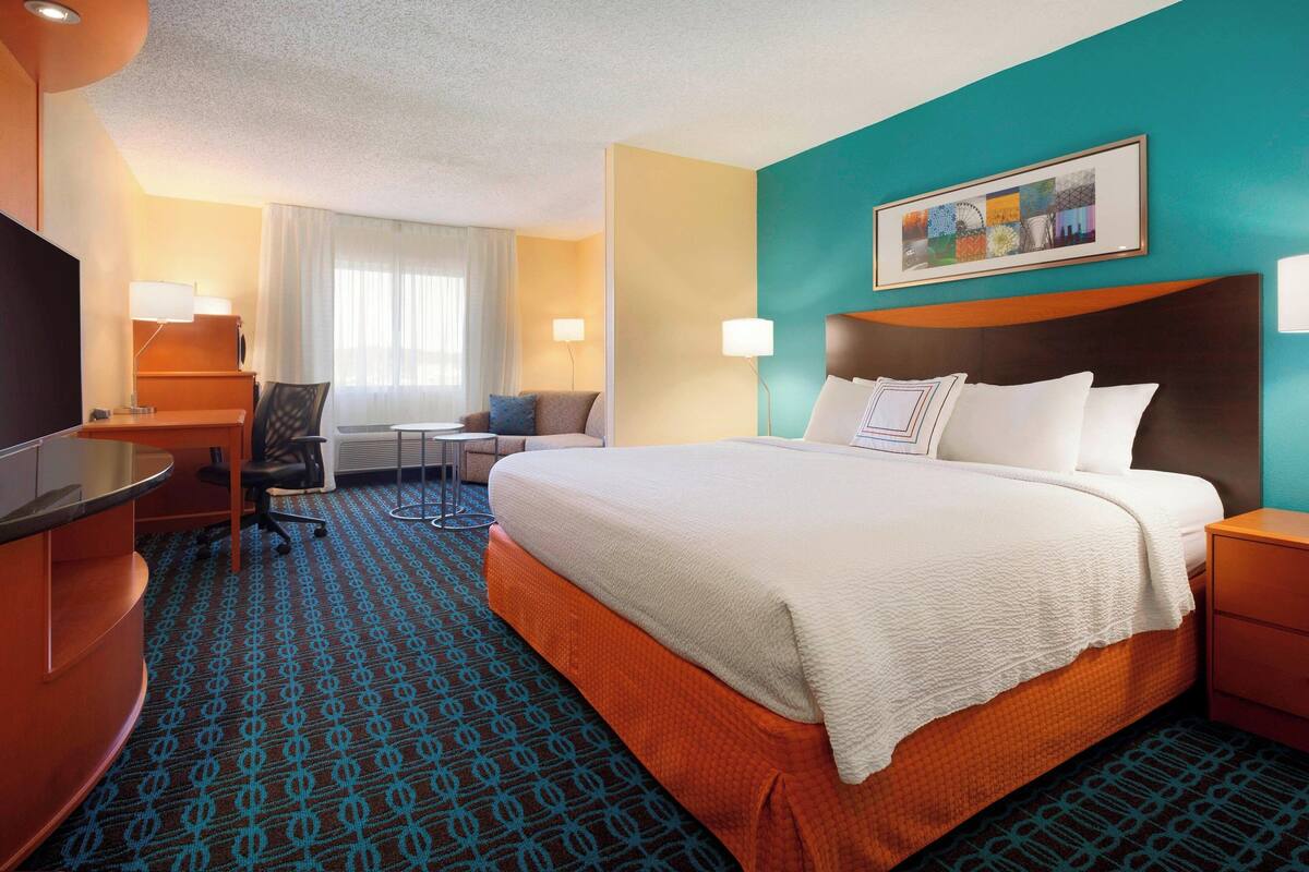 Ein Hotelzimmer mit einem großen Bett, einem Schreibtisch, einem Stuhl und einem Fernseher.