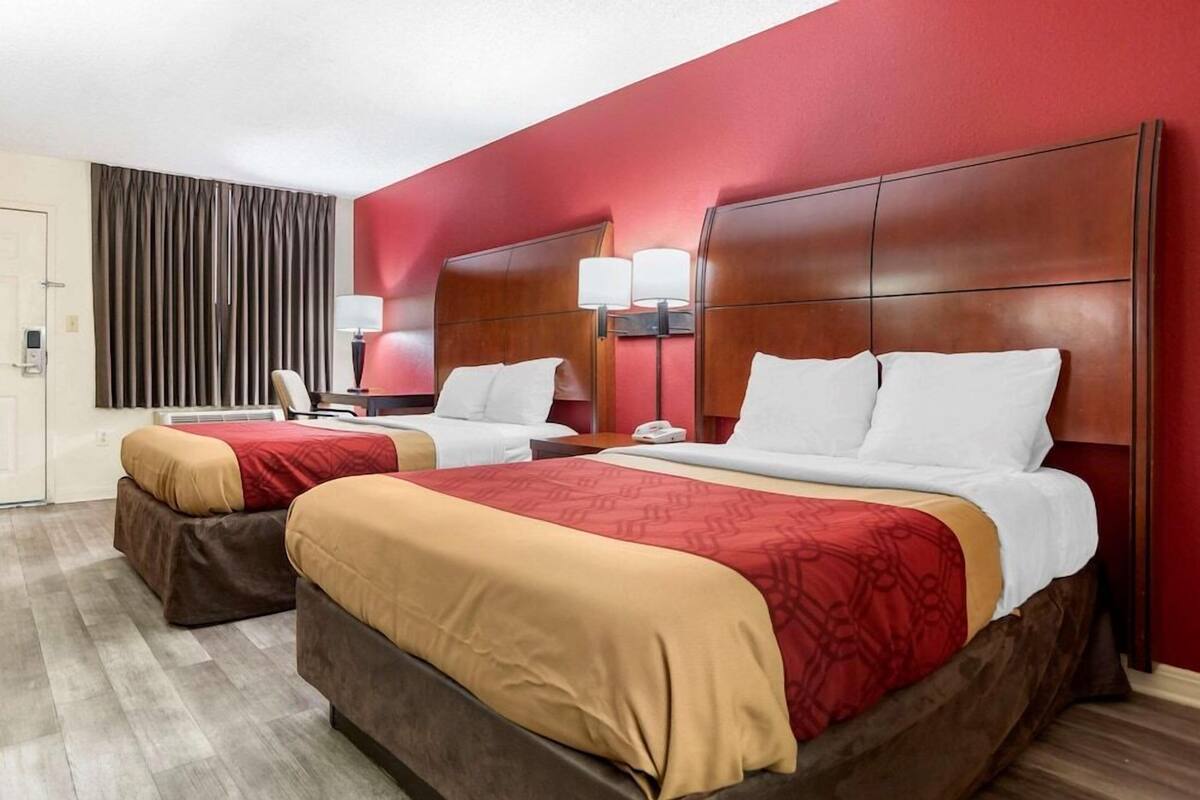A hotel room with two beds, a desk, a chair, a lamp, and a curtain.