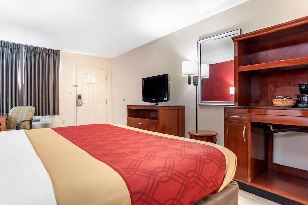 A hotel room with a bed, a television, a desk, a chair, a lamp, and a coffee machine.