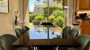 A modern kitchen with a glass dining table, wooden cabinets, and a view of a lush garden. - Shadow Mountain Resort (Palm Desert)