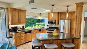 A modern kitchen with wooden cabinets, stainless steel appliances, and a central island with bar stools. - Shadow Mountain Resort (Palm Desert)