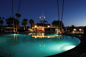 A nighttime pool area with palm trees, lounge chairs, and a building with lights. - Shadow Mountain Resort (Palm Desert)