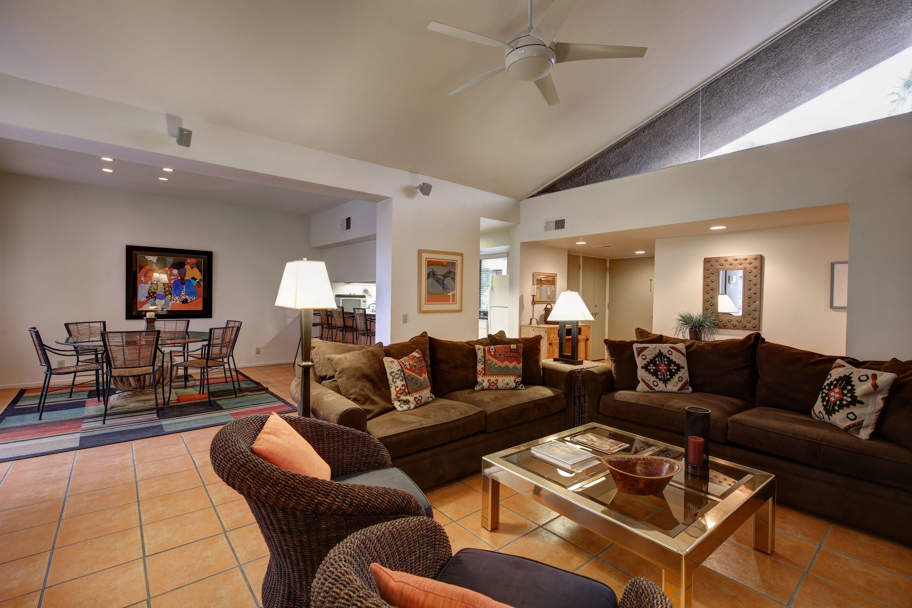 A spacious living room with a large brown sofa set, a coffee table, and a dining area with chairs and a table.
