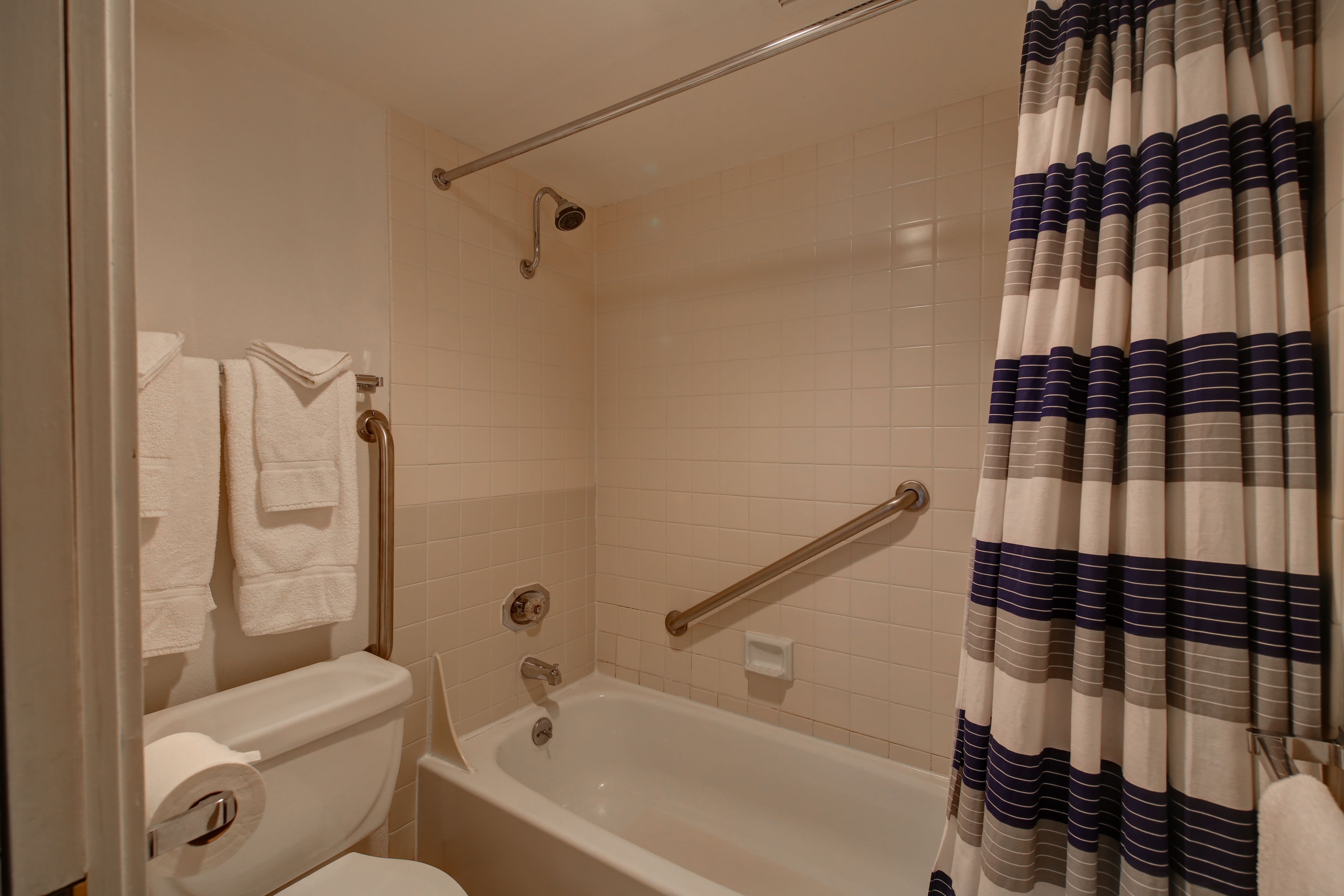 A bathroom with a bathtub, a shower, and a toilet. There are towels hanging on the wall and a striped shower curtain.