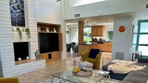 A spacious living area with a fireplace, a television, and a kitchen in the background. - Shadow Mountain Resort (Palm Desert)