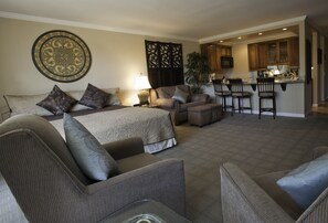 A spacious living area with a large bed, multiple seating options, a kitchen area, and a decorative wall piece. - Shadow Mountain Resort (Palm Desert)
