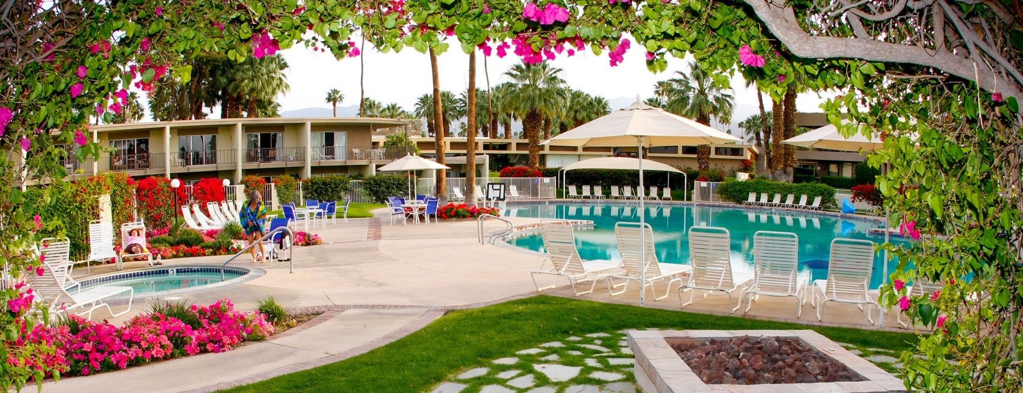 A pool area with lounge chairs, a hot tub, and a building with balconies.