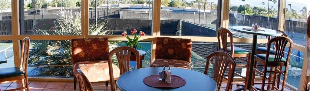 Un restaurante con vistas a una cancha de tenis, que cuenta con mesas y sillas redondas con tapicería floral.
