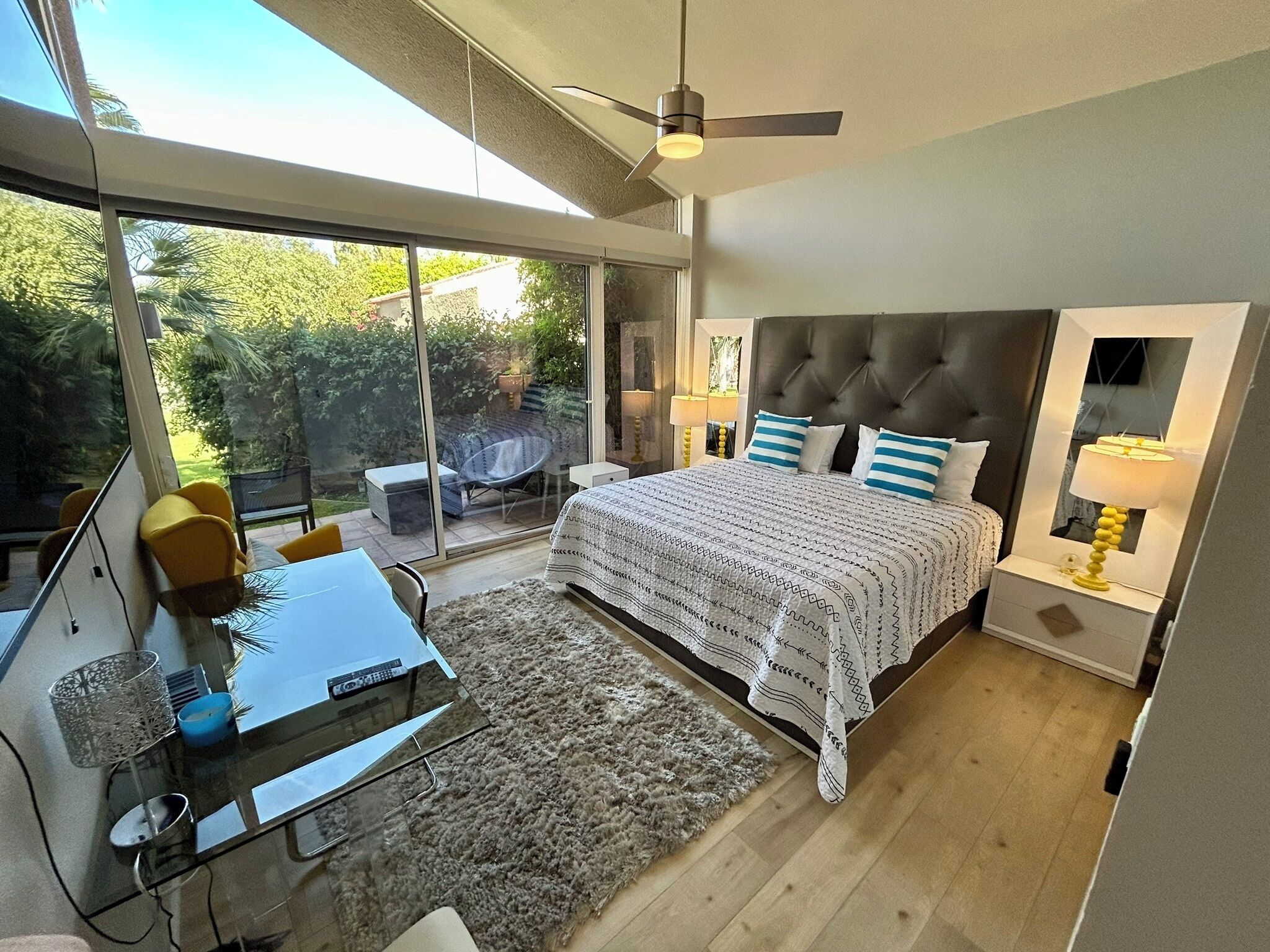 A modern bedroom with a large bed, a desk with a TV, and a view of the outdoors.