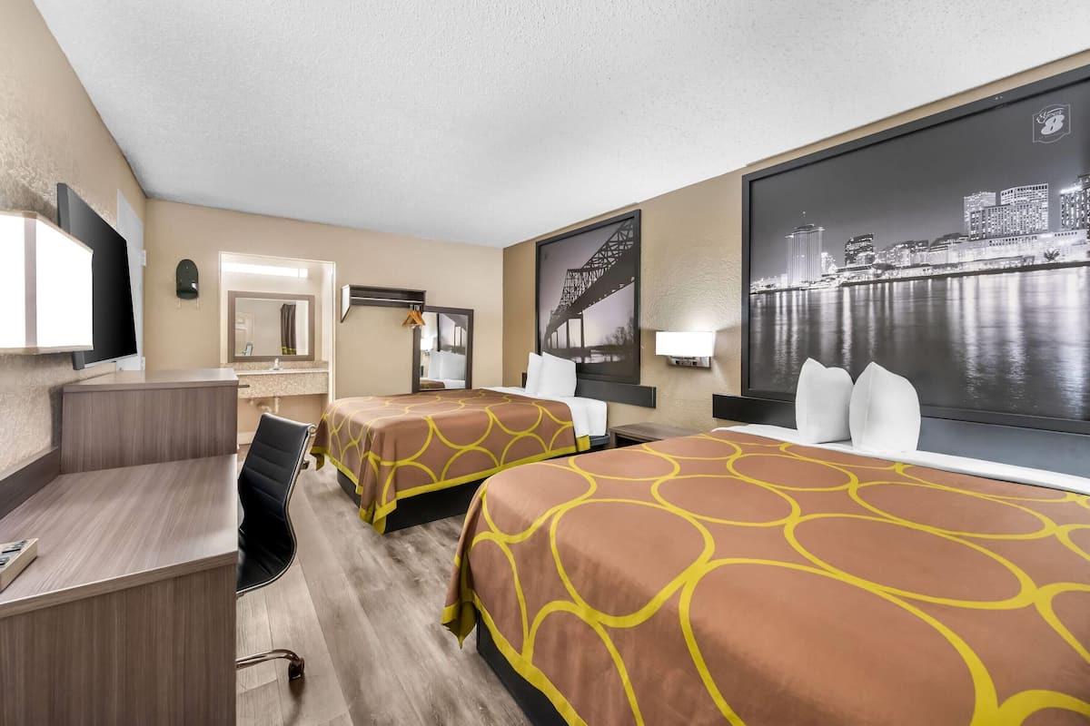 Une chambre d’hôtel avec deux lits, un bureau, un miroir et une grande fenêtre donnant sur le paysage urbain.