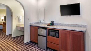 A compact hotel kitchen with a stainless steel refrigerator, built-in microwave, and a coffee maker.
