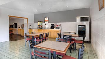 A modern kitchen with a built-in microwave, an ice dispenser, and a coffee machine. There are wooden tables and chairs with red cushions.
