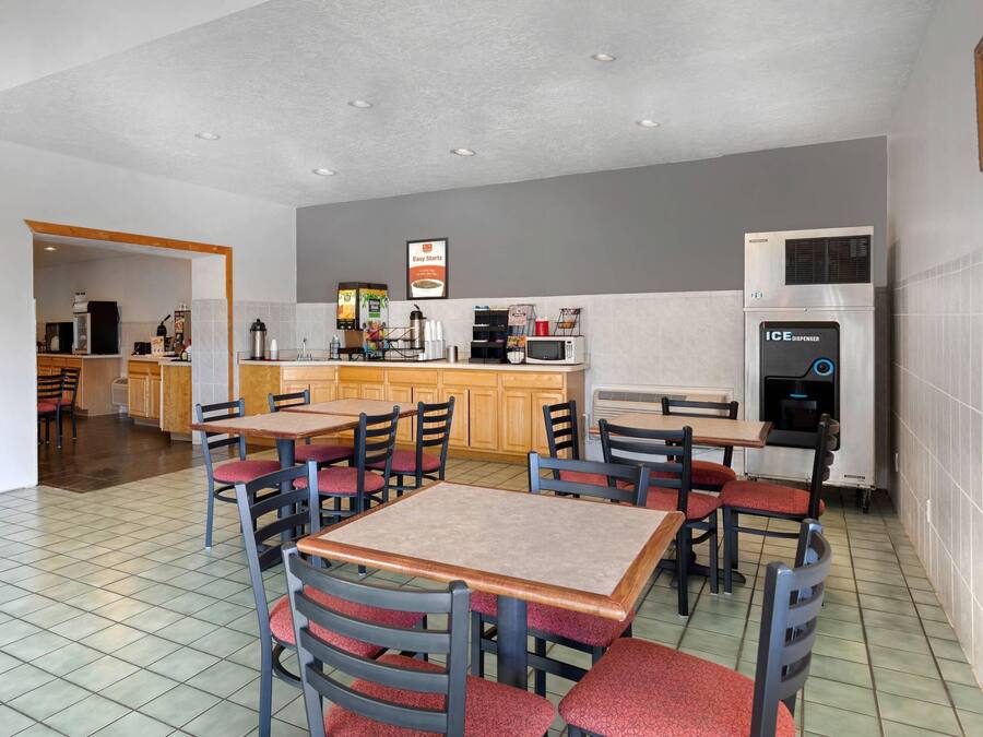 A modern kitchen with a built-in microwave, an ice dispenser, and a coffee machine. There are wooden tables and chairs with red cushions.