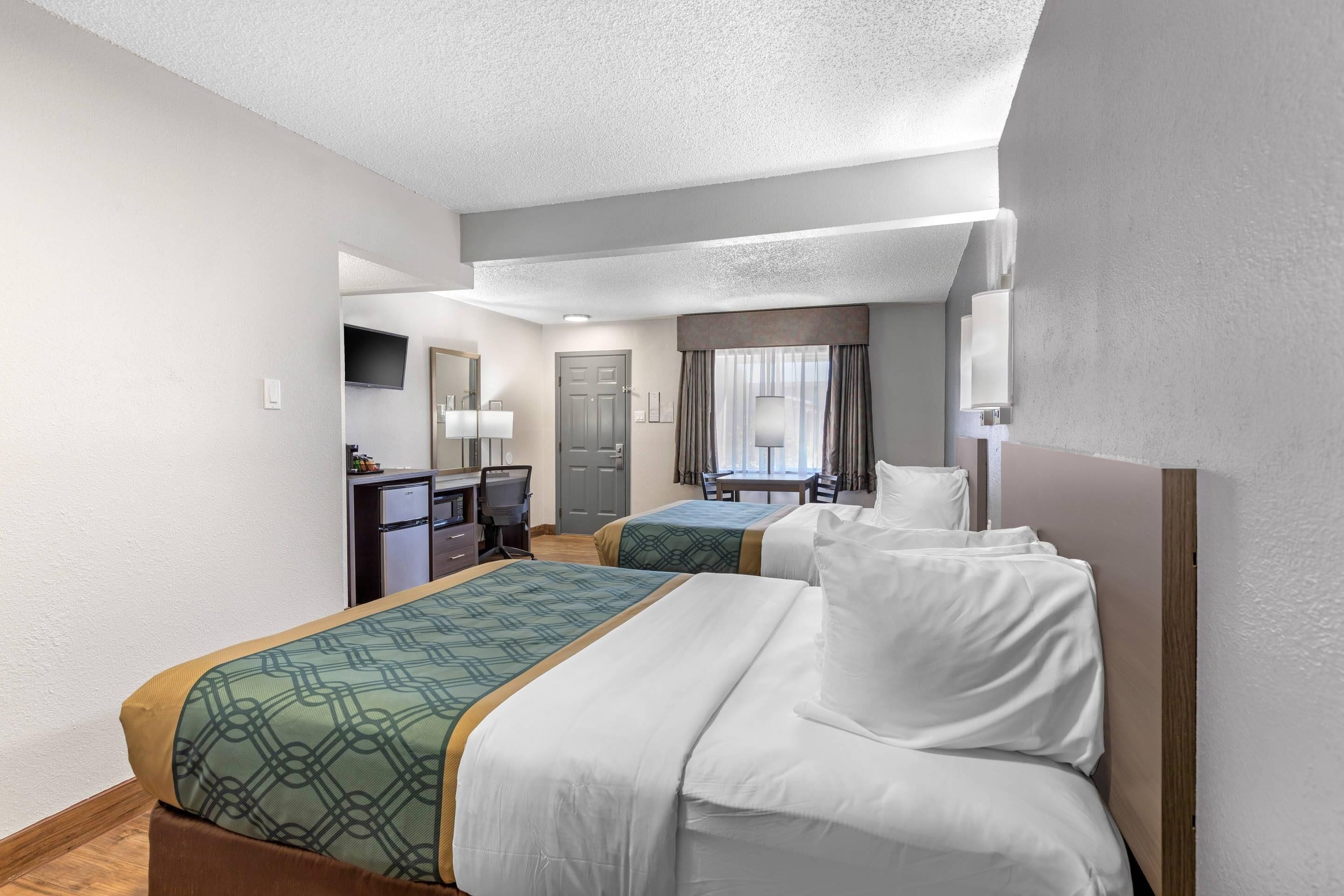 A hotel room with two beds, a desk, a chair, a television, and a window with curtains.