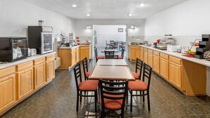 A modern kitchen with a central island, wooden cabinets, and a dining area with red upholstered chairs.