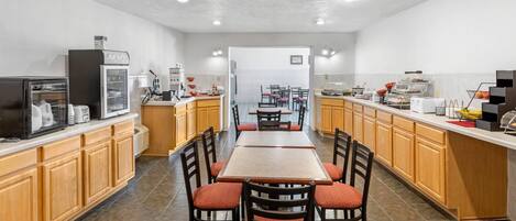 A modern kitchen with a central island, wooden cabinets, and a dining area with red upholstered chairs.