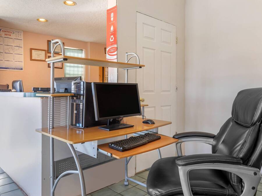 A small office with a desk, computer, keyboard, and a black leather chair.