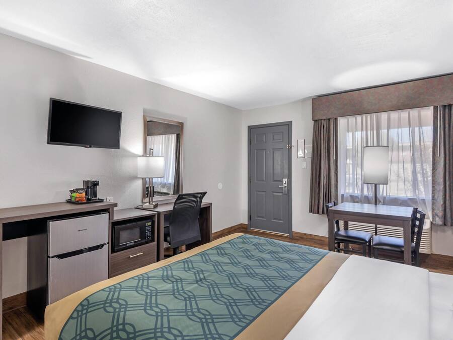 Habitación de hotel con cama, escritorio, kitchenette, televisión y ventana con cortinas.