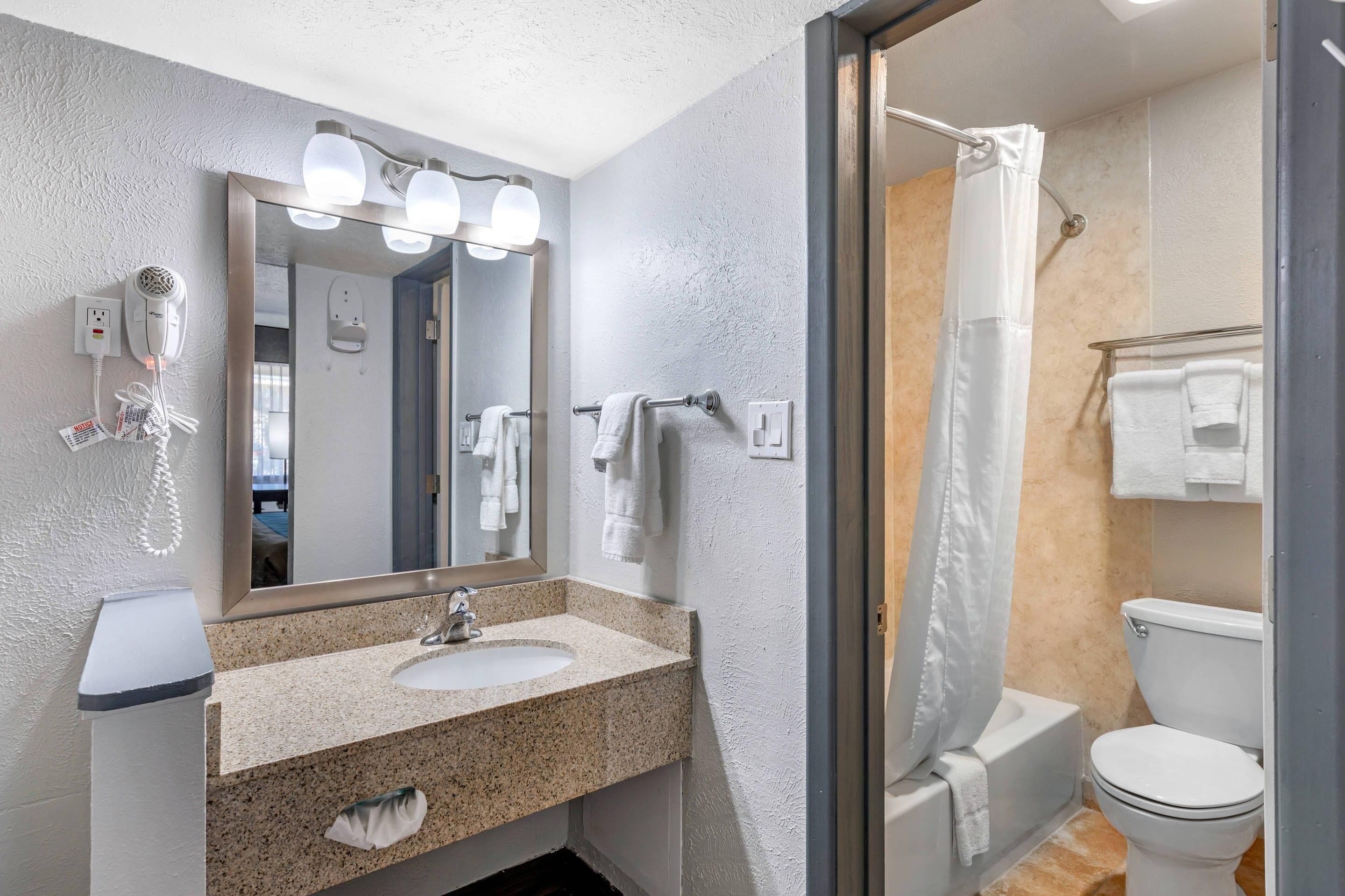 Un baño moderno con lavamanos de granito, un espejo grande, un secador de pelo y cortina de ducha.