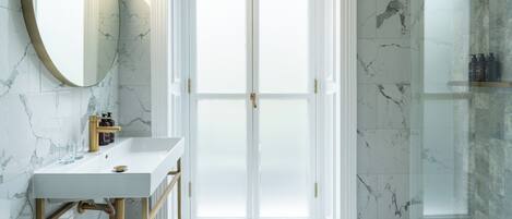 A modern bathroom with a marble wall, a large mirror, a white sink, and a glass shower enclosure.