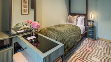 Quarto com cama de dossel, mesa de cabeceira com abajur, espelho e um vaso decorativo com flores.