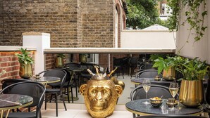Un café en plein air avec des tables et des chaises, une grande sculpture d’un ours doré et des plantes en pot.