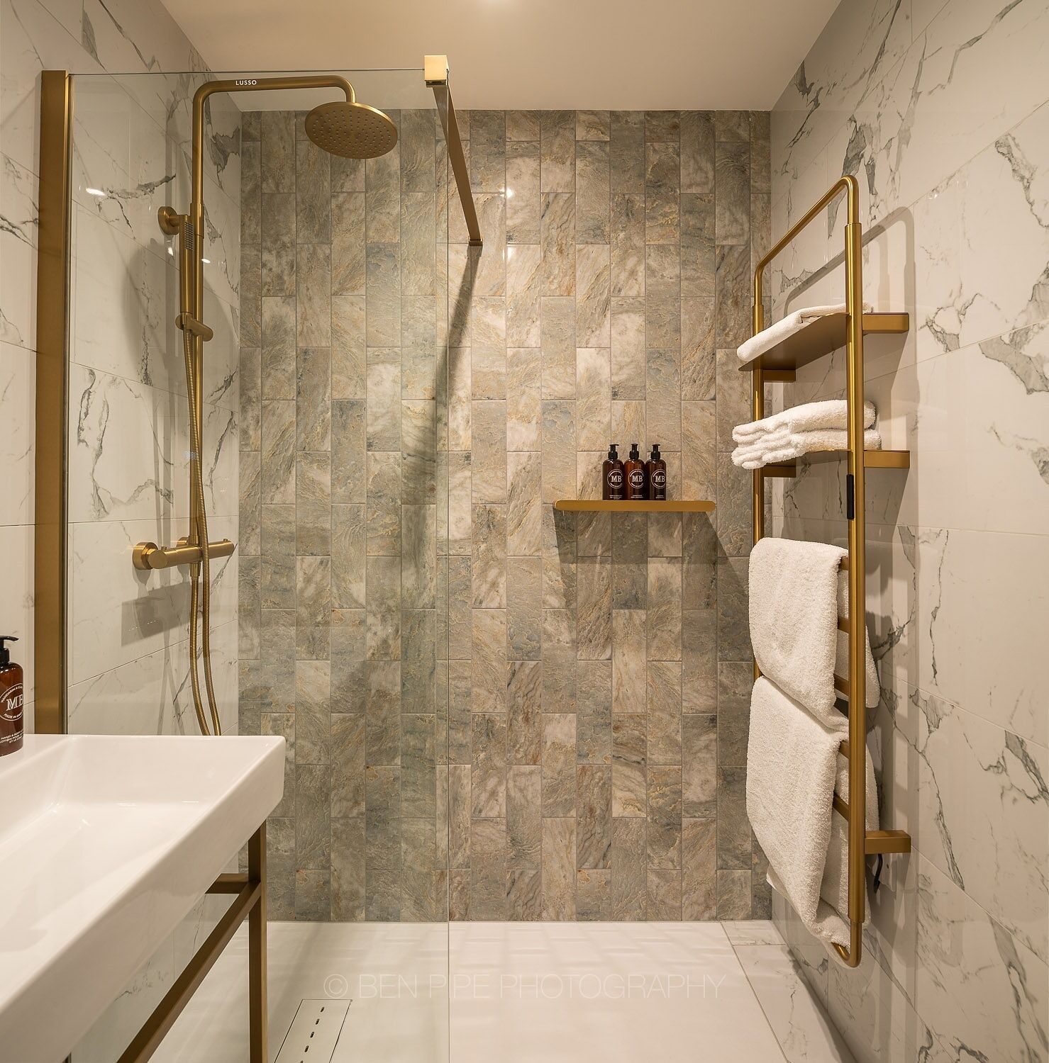 A modern bathroom with a marble shower, gold fixtures, and a towel rack.