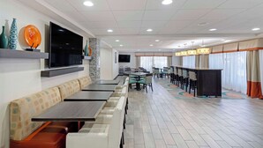 A modern restaurant with long communal tables and booths, a flat-screen TV mounted on the wall, and a patterned floor. - Best Western Plus Chicagoland - Countryside (Countryside)