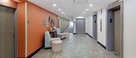 A hotel corridor with orange walls, a herringbone-patterned floor, and a row of doors on the right.