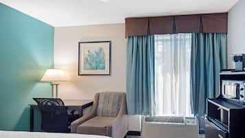 Una habitación de hotel con cama, escritorio con lámpara, silla, televisor y aire acondicionado.