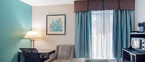 Una habitación de hotel con cama, escritorio con lámpara, silla, televisor y aire acondicionado.