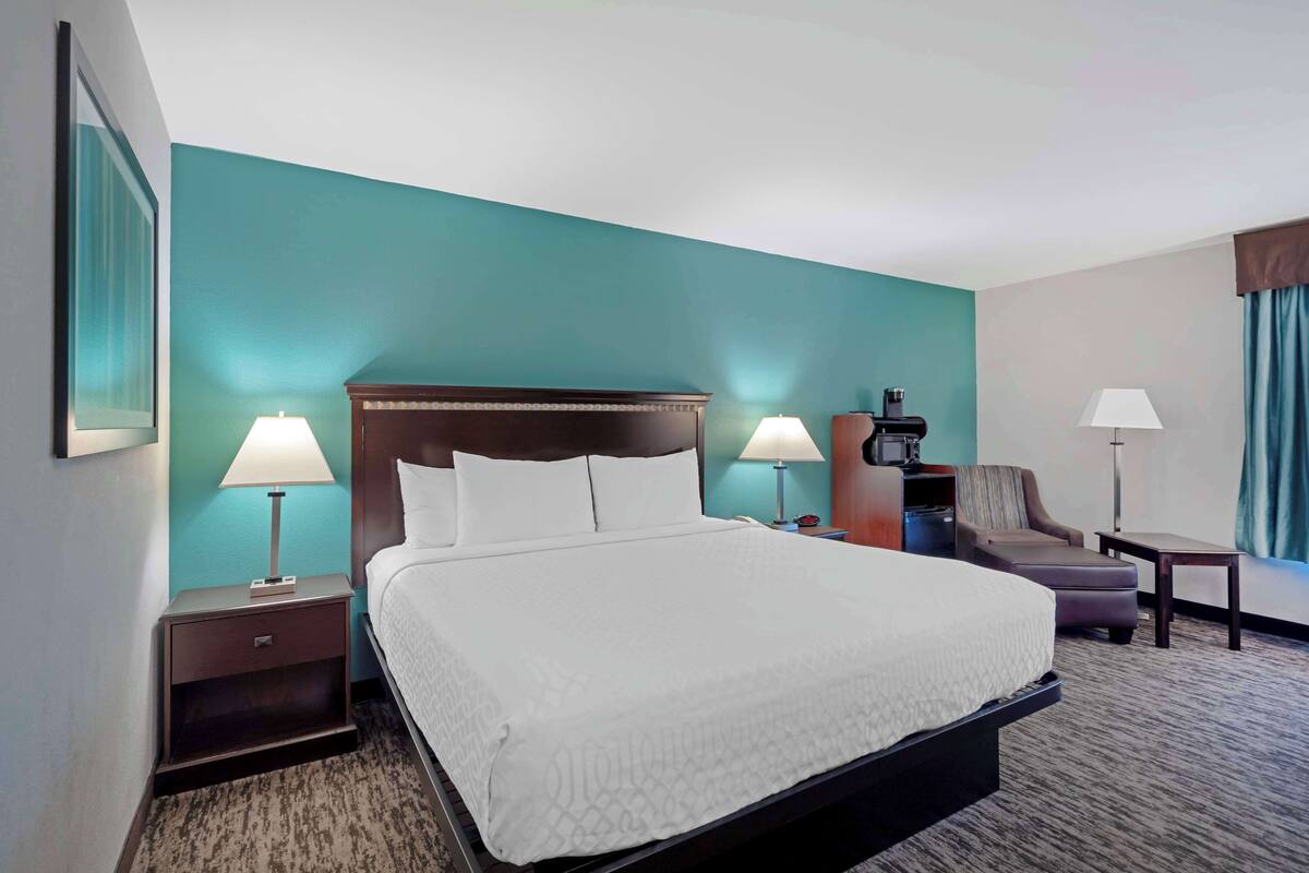 A hotel room with a large bed, two bedside tables with lamps, a desk with a chair, and a view of the city.