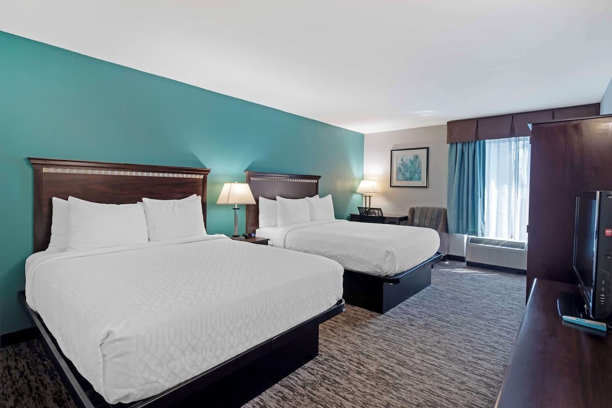A hotel room with two beds, a desk with a television, a chair, and a window with curtains.