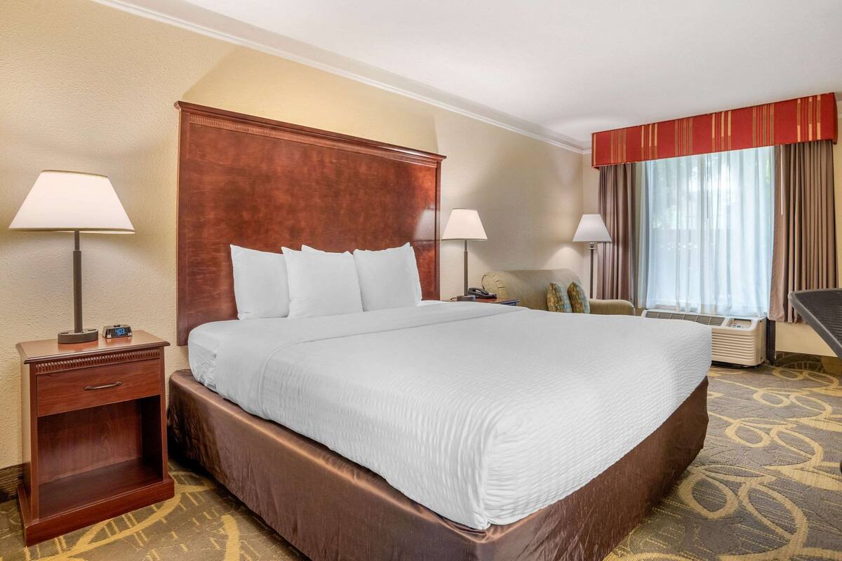A hotel room with a large bed, two bedside tables with lamps, a chair, and a window with curtains.