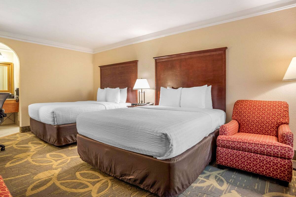 A hotel room with two beds, a red patterned armchair, and a patterned carpet.