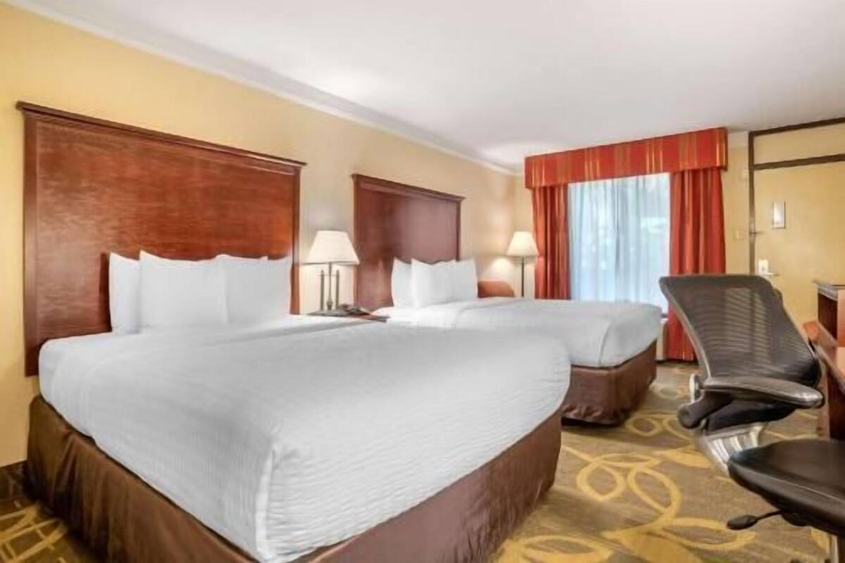 A hotel room with two beds, a desk, a chair, and a window with curtains.