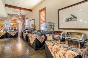 A buffet setup with multiple serving stations, a brick archway, and framed artwork on the walls.