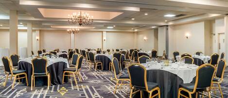 A large banquet hall with round tables, black and gold chairs, and a patterned carpet.