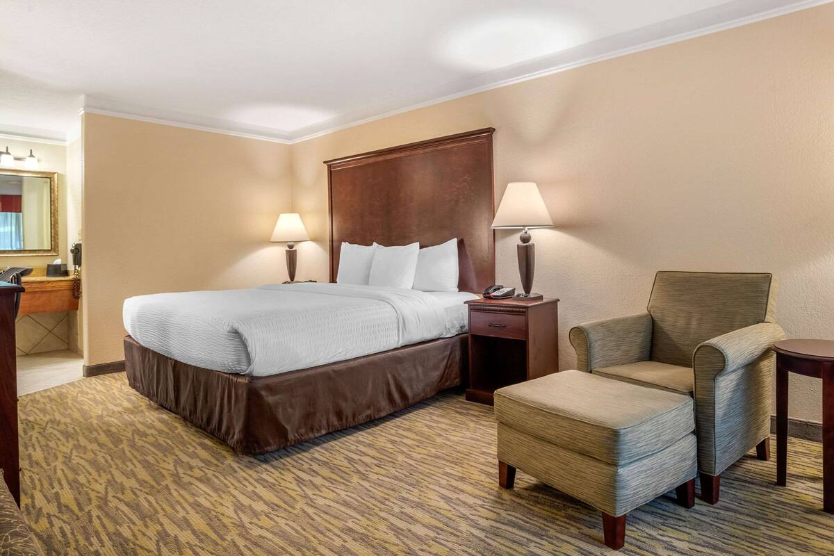 A hotel room with a large bed, two bedside lamps, a chair, a desk, and a mirror.