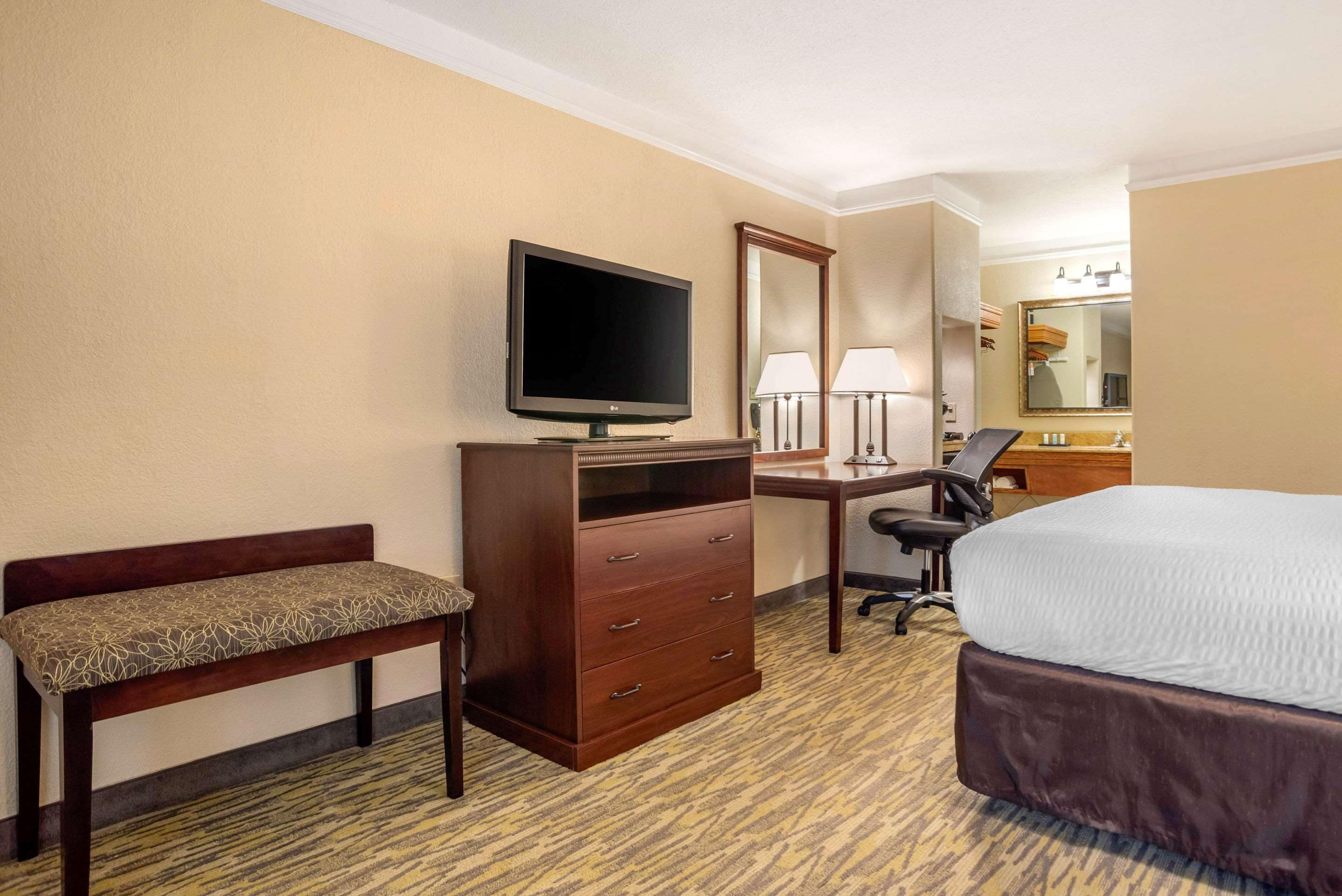 Une chambre d’hôtel comprenant un lit, un bureau avec un ordinateur, une télévision, une chaise, un banc et une commode.
