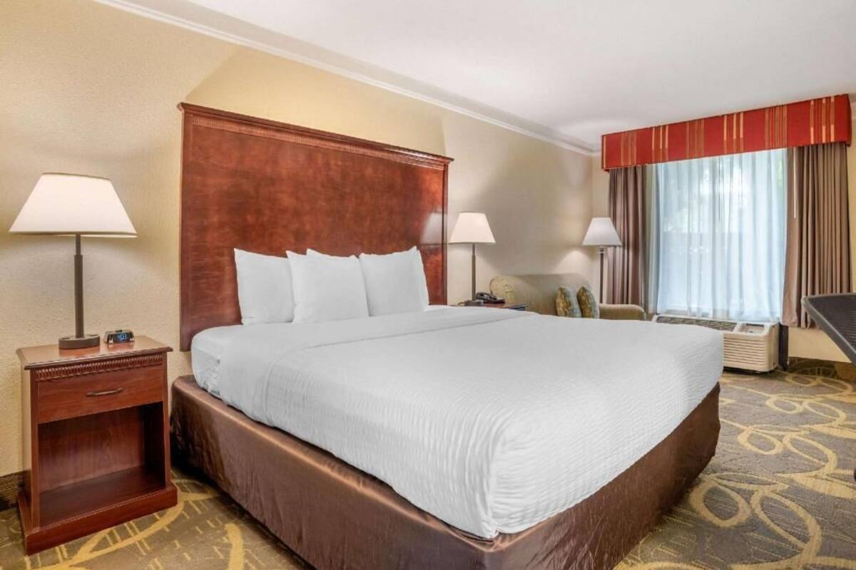 A hotel room with a large bed, two bedside tables, a chair, a desk, and a window with curtains.