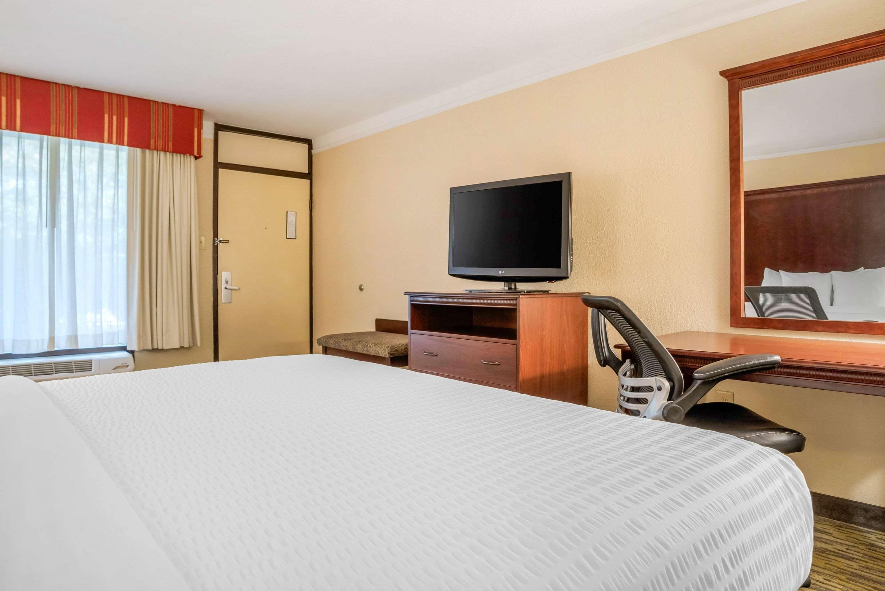 Una camera d'albergo con un letto grande, una televisione su un mobile in legno, una scrivania con una sedia e una finestra con tende.