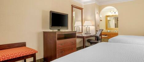 A hotel room with two beds, a desk with a computer, a TV, a chair, a desk lamp, and a mirror.
