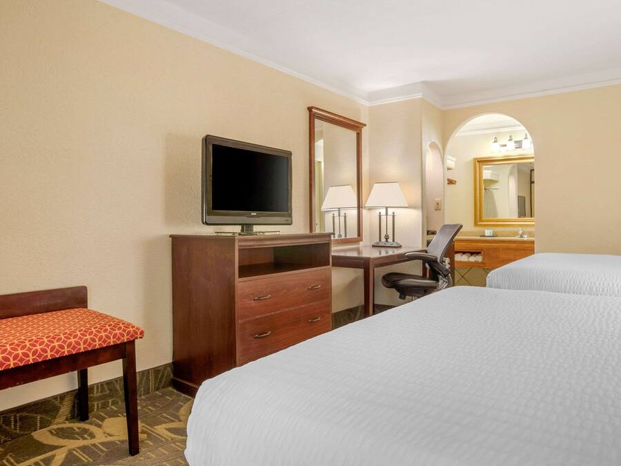 A hotel room with two beds, a desk with a computer, a TV, a chair, a desk lamp, and a mirror.