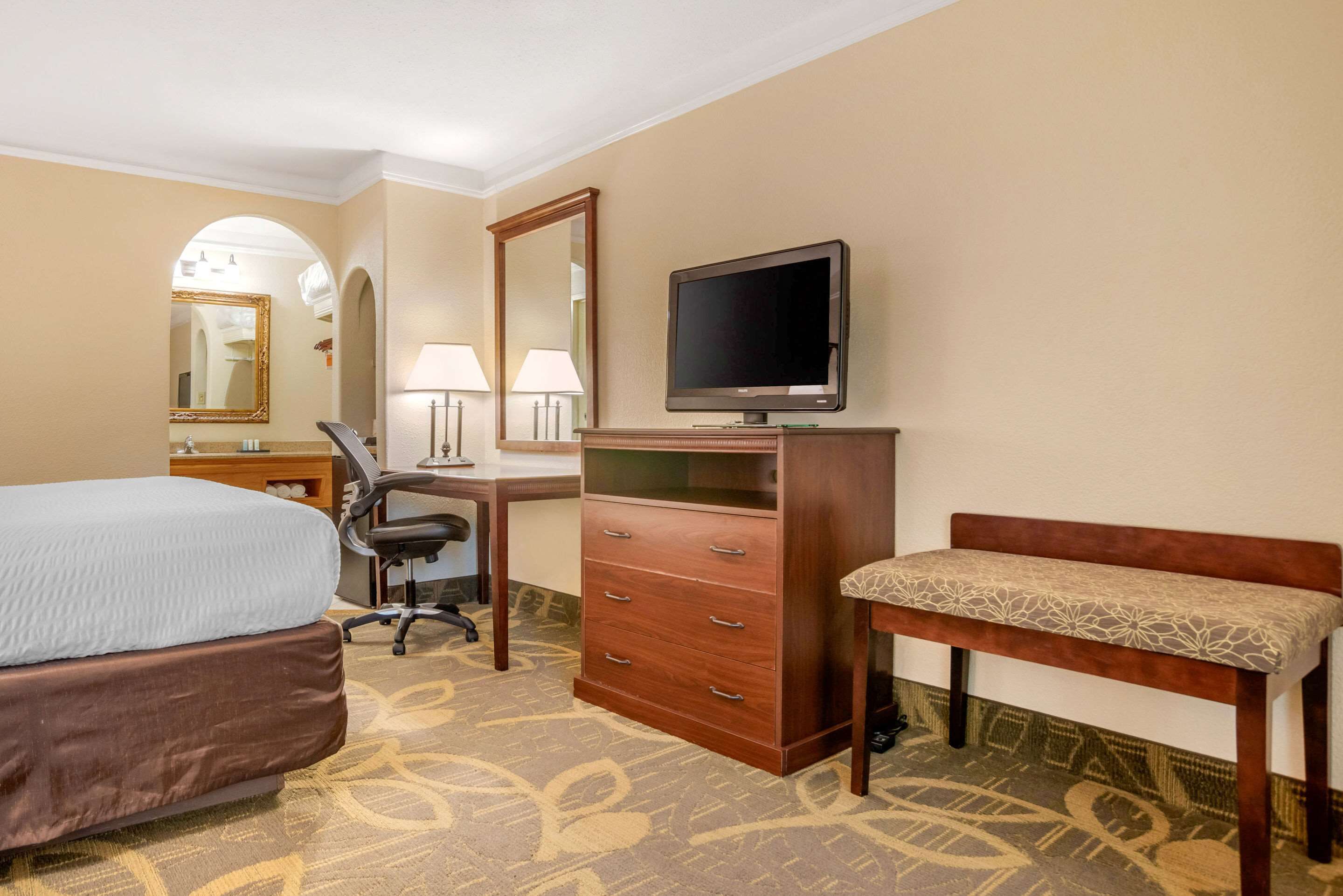 Ein Hotelzimmer mit Bett, Schreibtisch, Stuhl, Fernseher, Kommode und Sitzbank.