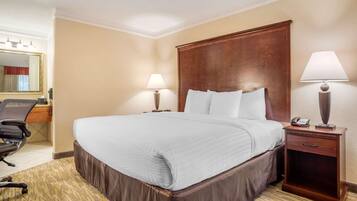 A hotel room with a large bed, two bedside lamps, a wooden nightstand, a desk with a chair, and a mirror.