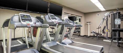 Un gimnasio con cintas de correr, máquinas de pesas y una pantalla de televisión en la pared.