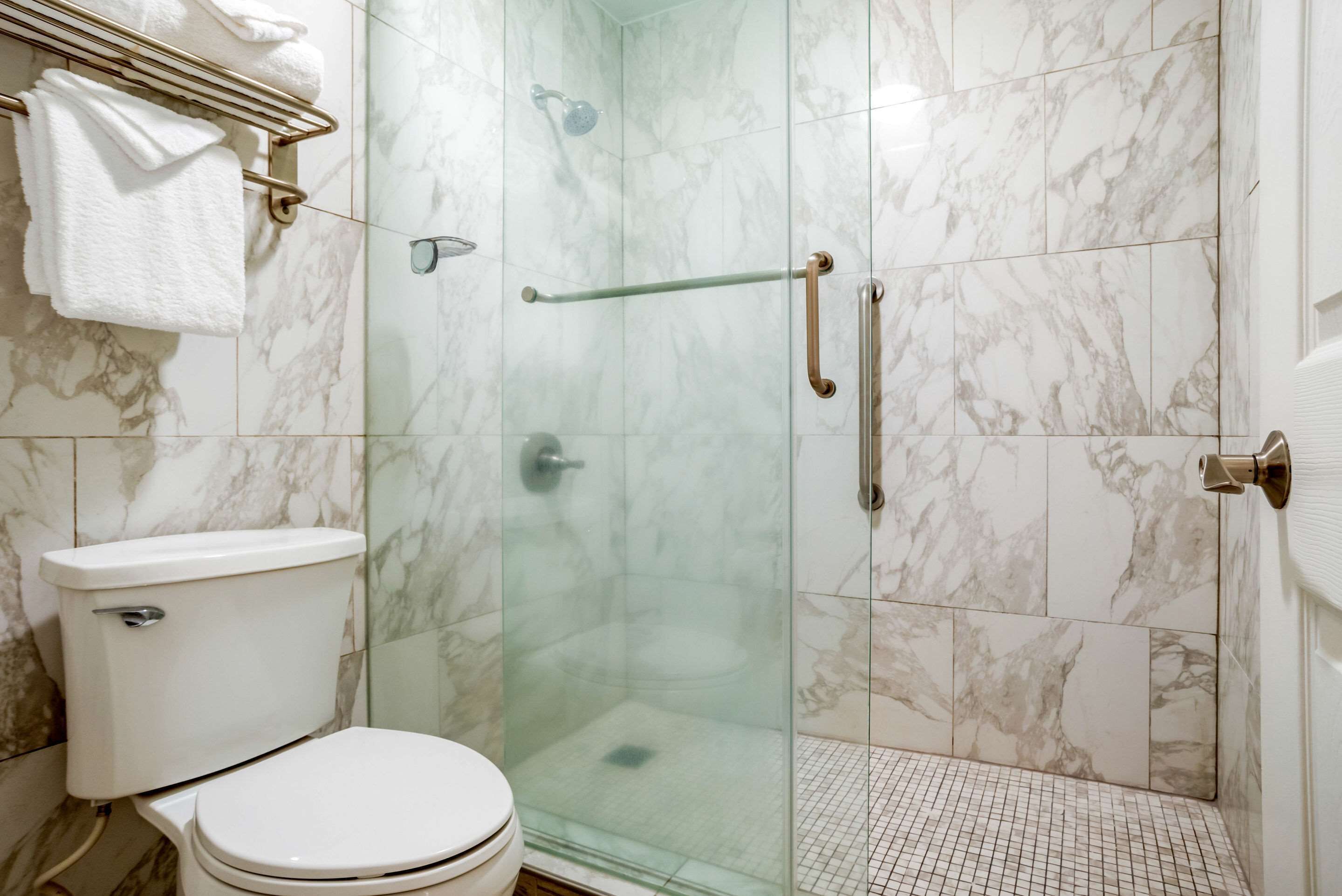 Un baño con ducha de vidrio, inodoro y pisos de mármol.